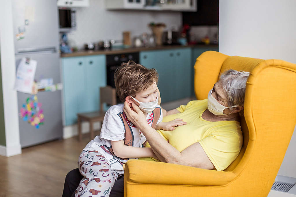 A grandparent playing with their grandchild both wearing masks