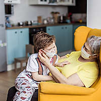 A grandparent playing with their grandchild both wearing masks