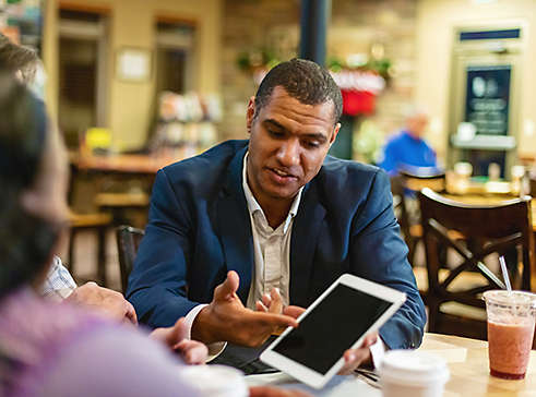 A man showing someone something on his ipad in a cafe