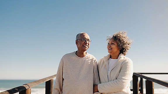 A couple standing on a boardwalk by the beach