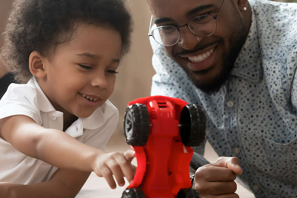 Father and son play with red race car toy