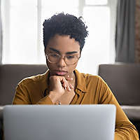 African woman in glasses sitting at desk staring at laptop screen
