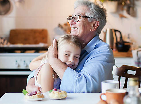 Grandmother hugging granddaughter in kitchen.