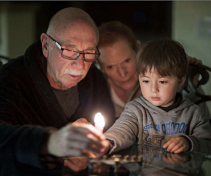 A young child and grandparents lighting candles together