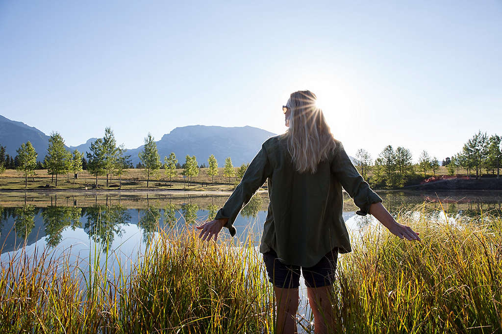 Woman with her arms extended next to a mountain lake.