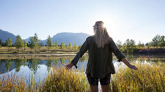 Woman with her arms extended next to a mountain lake.