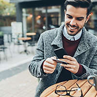 A man using his credit card while on his cell phone.