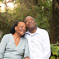 Older couple sitting outdoors among trees.