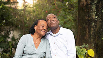 Older couple sitting outdoors among trees.