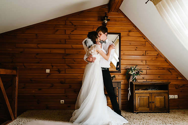 Bride and groom hugging and kissing indoors.