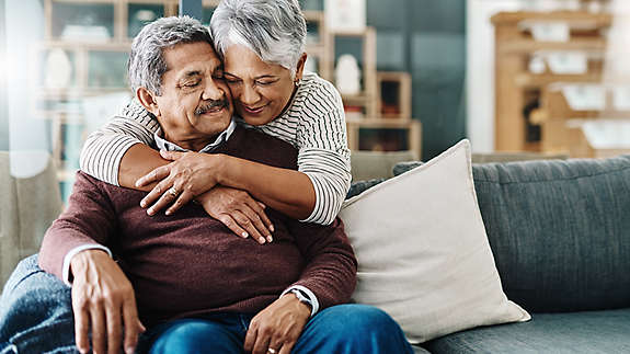 A mature couple hugging each other on the couch.