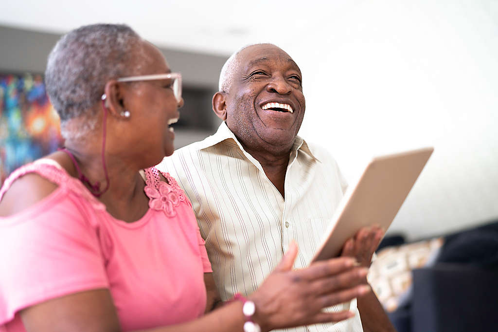 A mature couple laughing and smiling at something on a tablet.