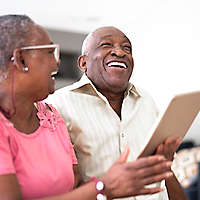 A mature couple laughing and smiling at something on a tablet.