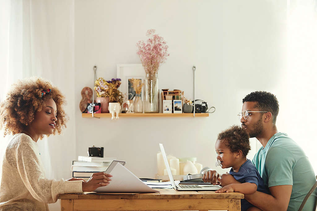 A young couple sitting at the table reviewing paperwork with their baby.