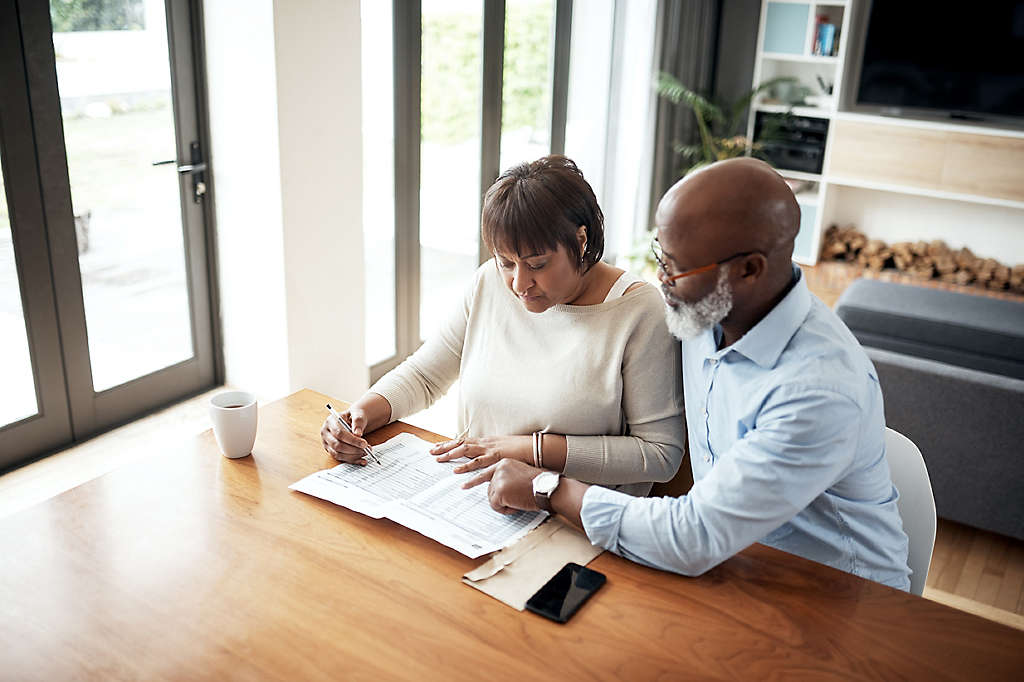 A mature couple at home sitting at a table looking over a spreadsheet. 