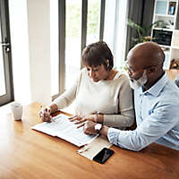 A mature couple at home sitting at a table looking over a spreadsheet. 