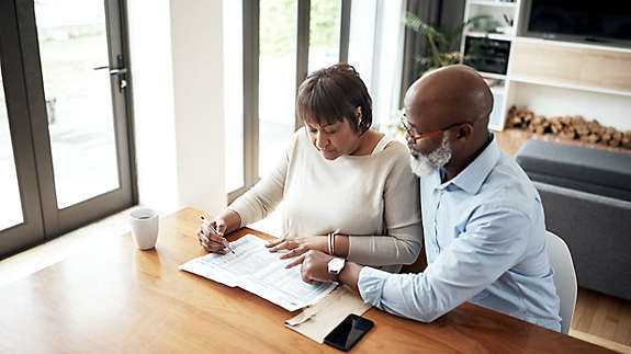 A mature couple at home sitting at a table looking over a spreadsheet.