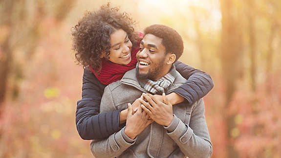 A young woman hugging a young man from behind while walking outside.