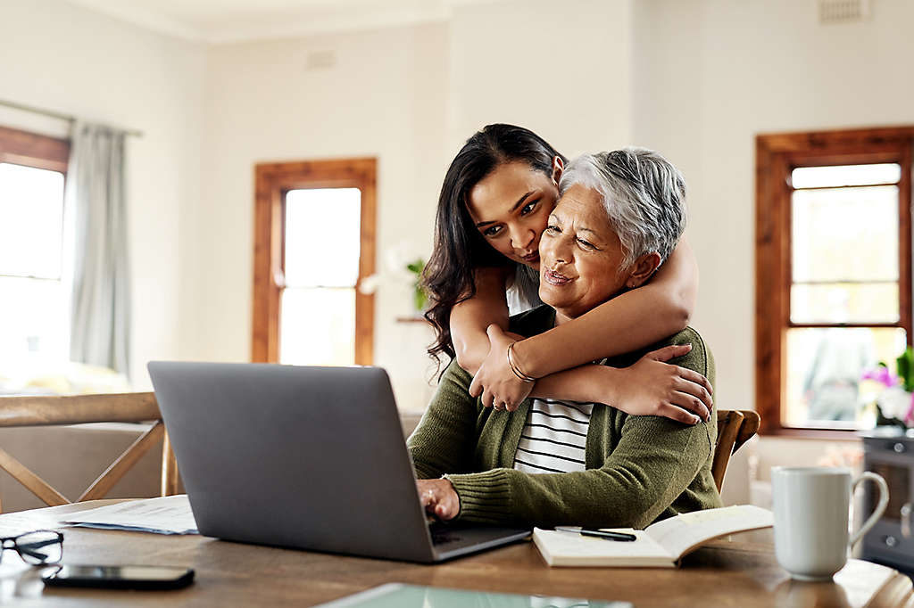 A mature woman being hugged by an older child while working on a computer.