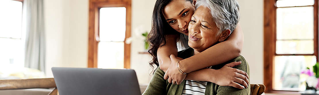 A mature woman being hugged by an older child while working on a computer.