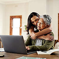 A mature woman being hugged by an older child while working on a computer.