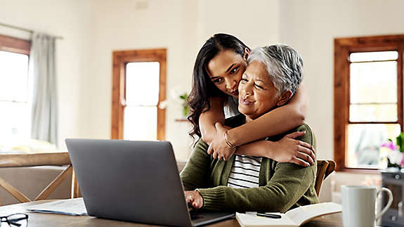 A mature woman being hugged by an older child while working on a computer.