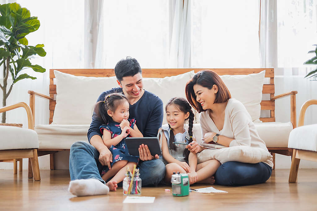 A young family sitting on the floor of their living room looking at a tablet.