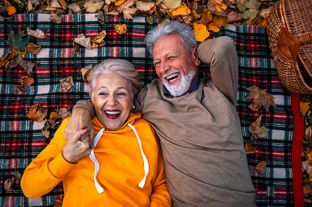 A mature couple laying on a picnic blanket laughing.