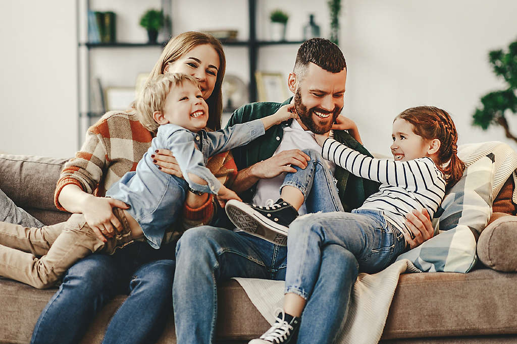 A young family playing together at home on the couch.