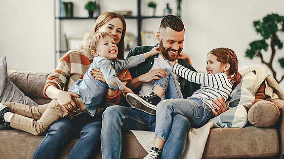 A young family playing together at home on the couch.