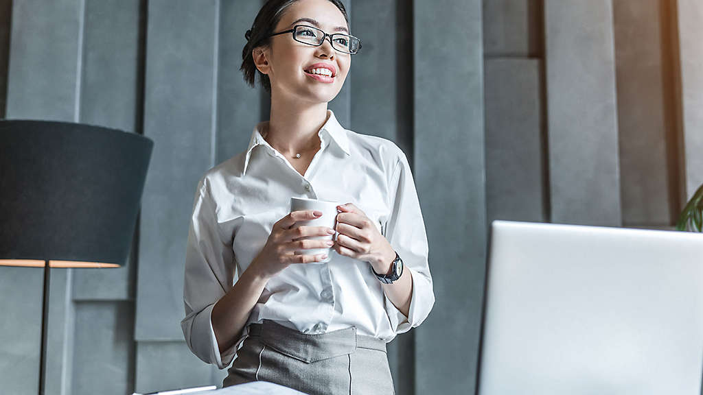 Woman in her office, smiling and holding a cup of coffee.