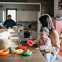 Mother holding a child while working on computer.