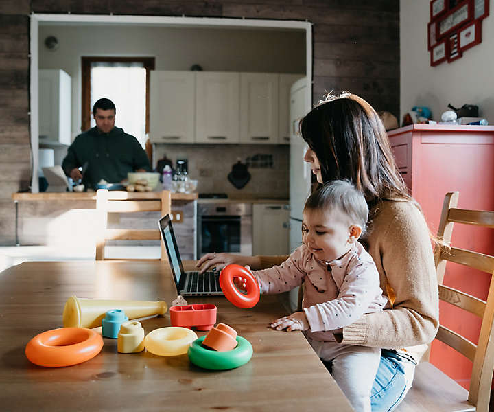 Mother holding a child while working on computer.