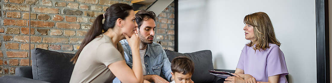 A young family sitting on a couch talking to an agent.
