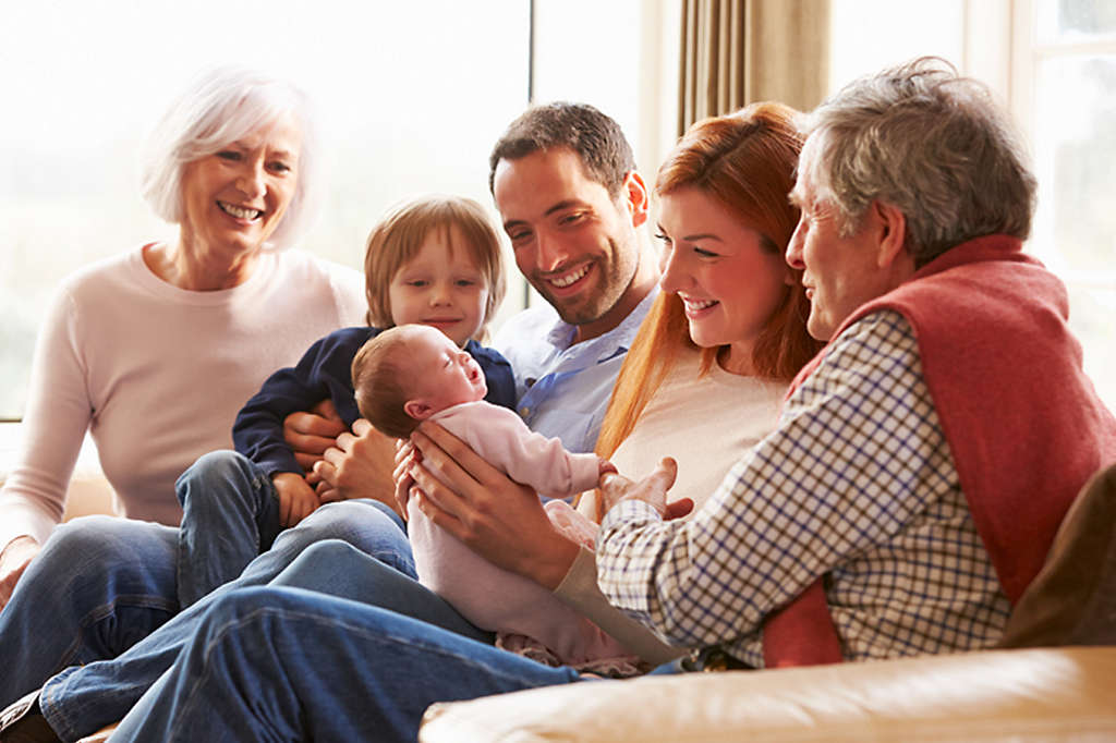 Multigenerational family across many ages sitting on a couch smiling at a newborn baby