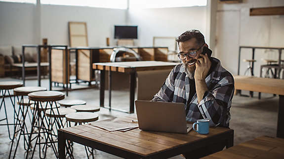 A man talking on his cell phone looking at something on his laptop computer.