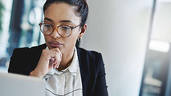 A woman wearing glasses looking at a computer screen. 