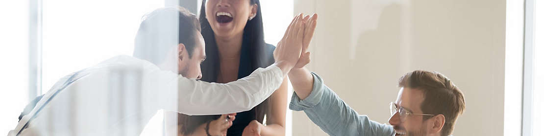 Employees at work celebrating and giving each other a high five at a meeting.
