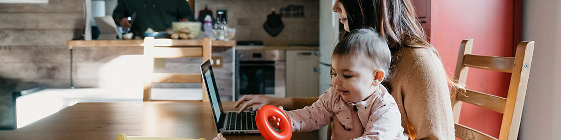 Mother holding a child while working on computer.