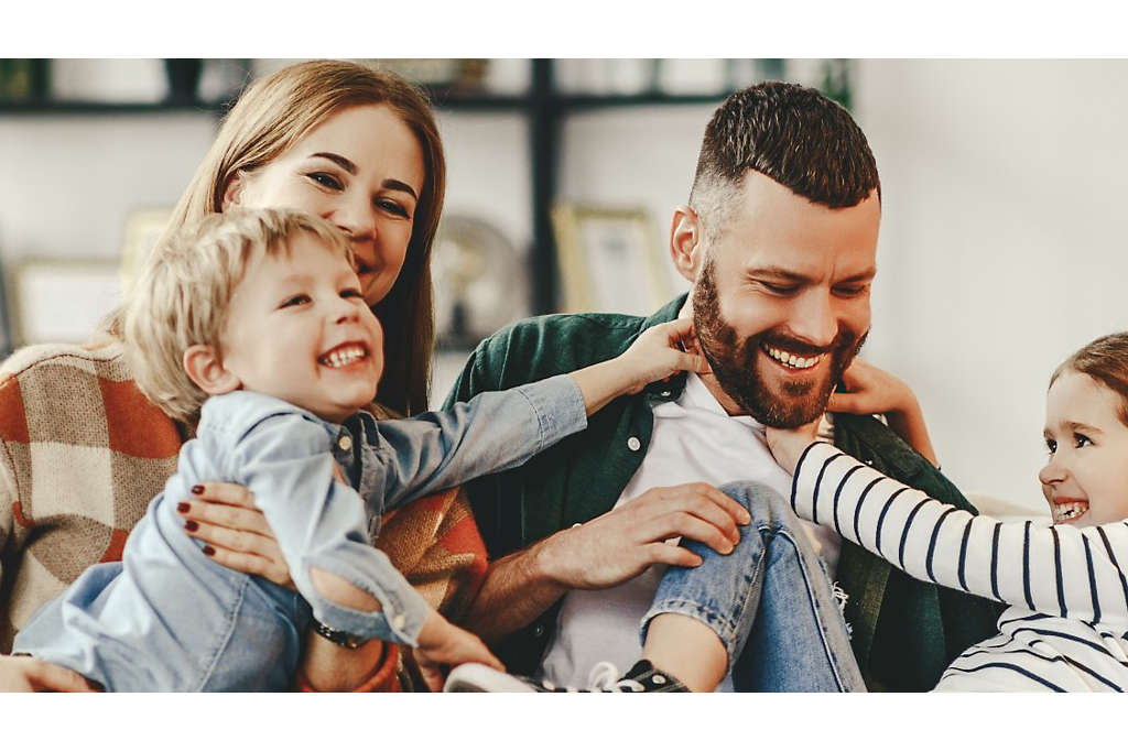 A young family playing together at home on the couch.