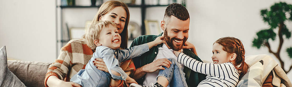 A young family playing together at home on the couch. 