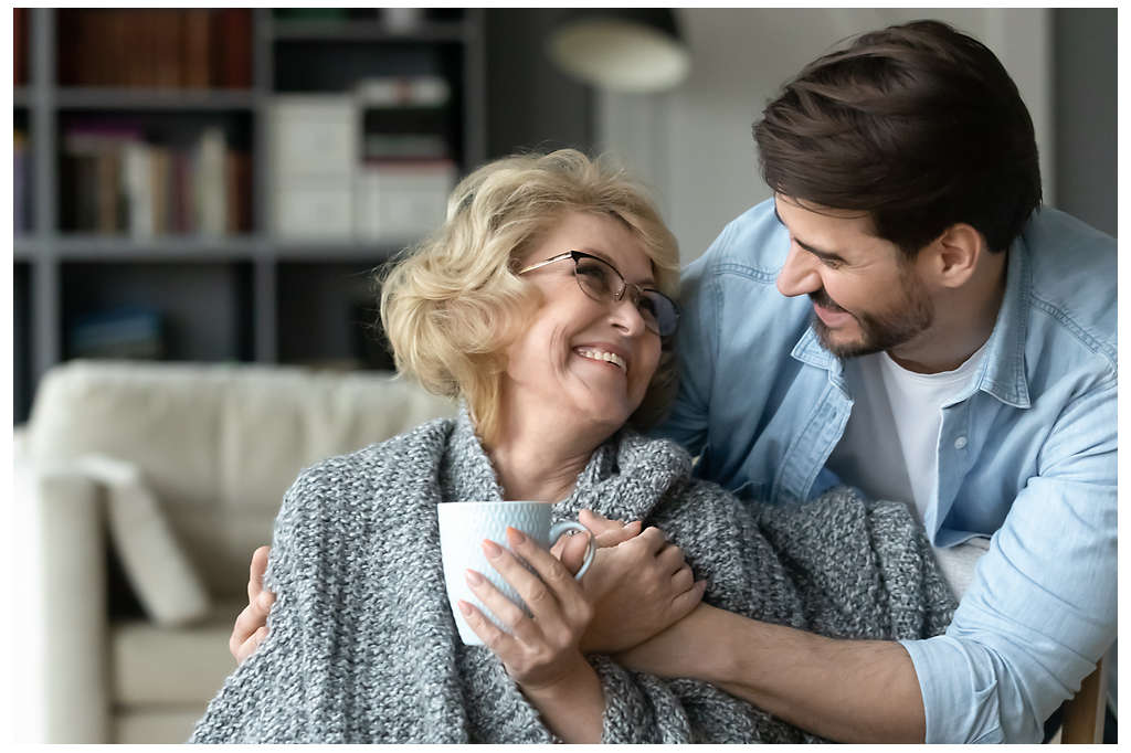 An older son smiling and hugging his elderly mother