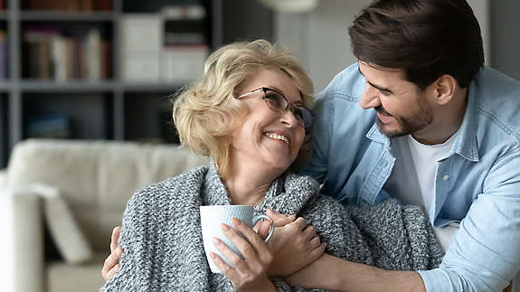 An older son smiling and hugging his elderly mother