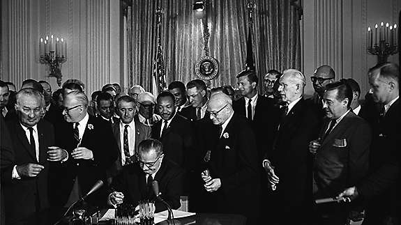 President Lyndon B. Johnson signs the 1964 Civil Rights Act as Dr. Martin Luther King, Jr. and others look on.
