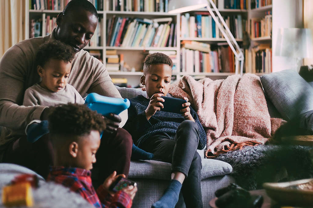 Man with 3 children in living room gathered around portable electronic devices