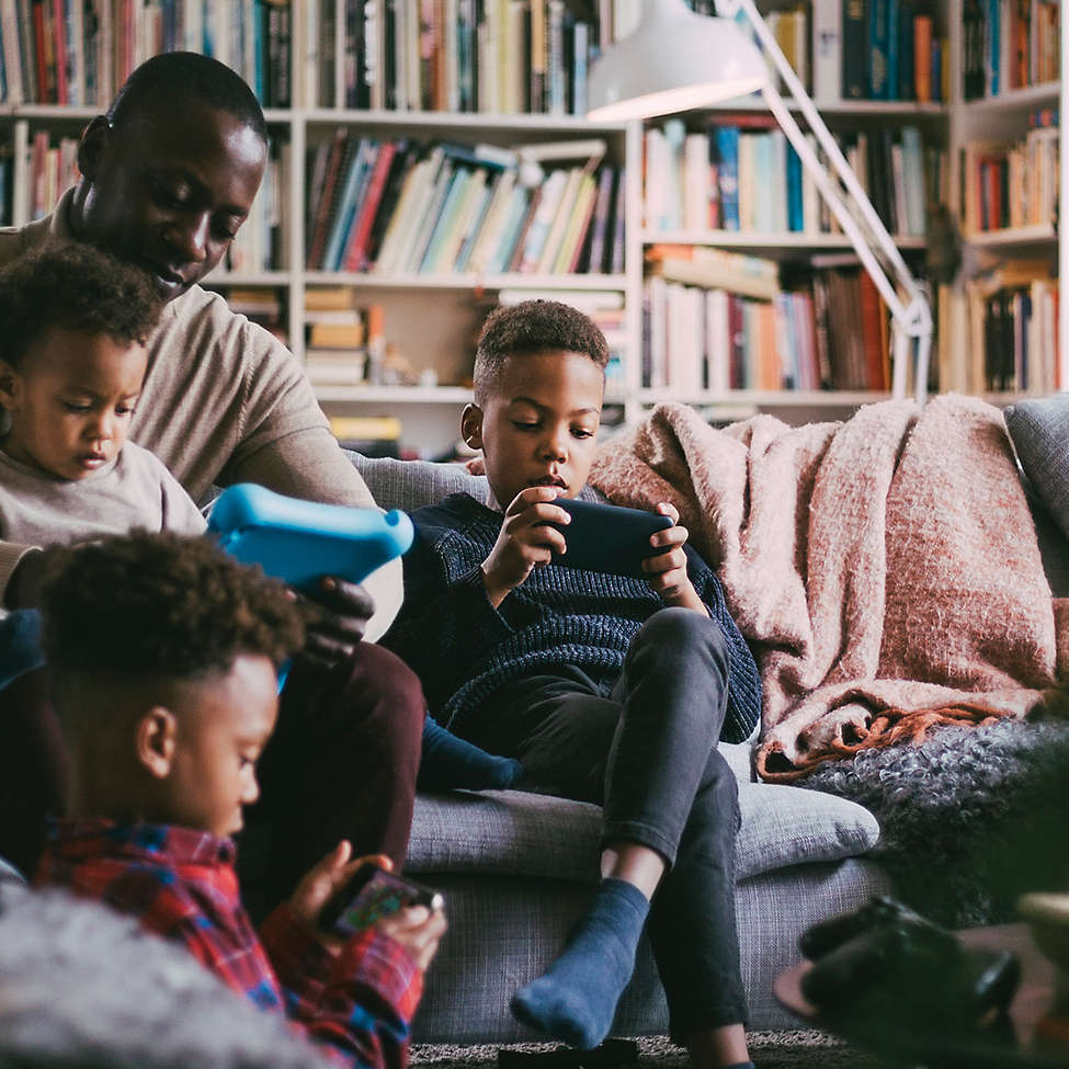 Man with 3 children in living room gathered around portable electronic devices