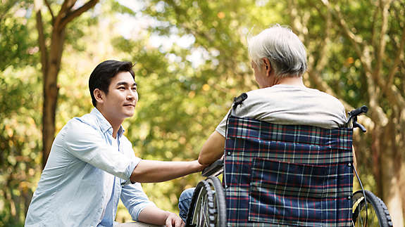 A man holding the hand of his father in a wheelchair