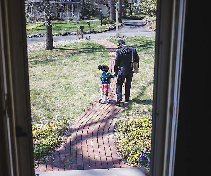 Father holding hands with his young daughter in their front yard before leaving for work