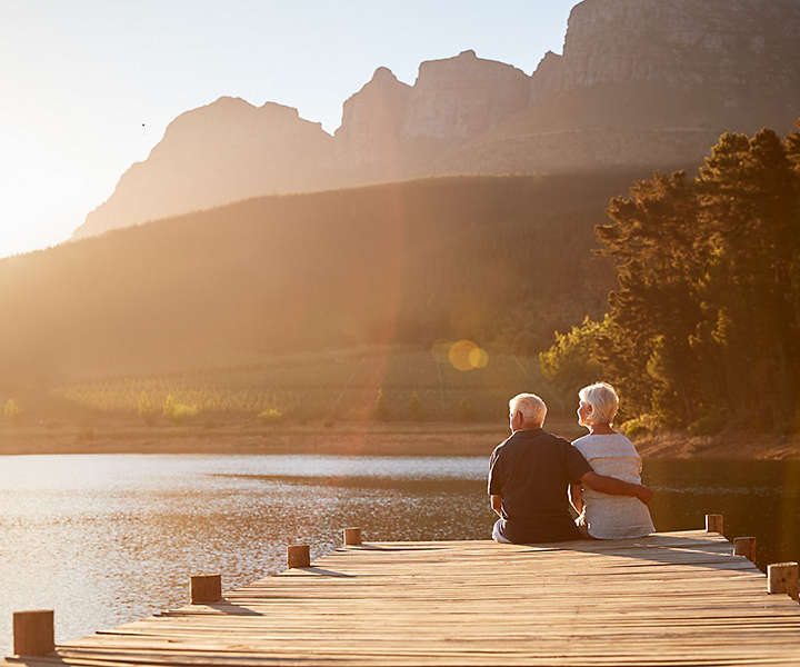 Senior Couple Sitting On Wooden Dock By Lake