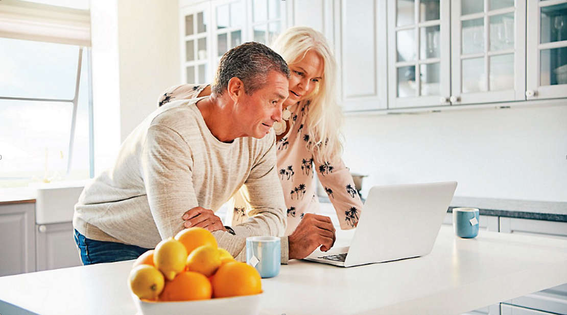 Couple looking at Long Term care options on a laptop in their kitchen.
